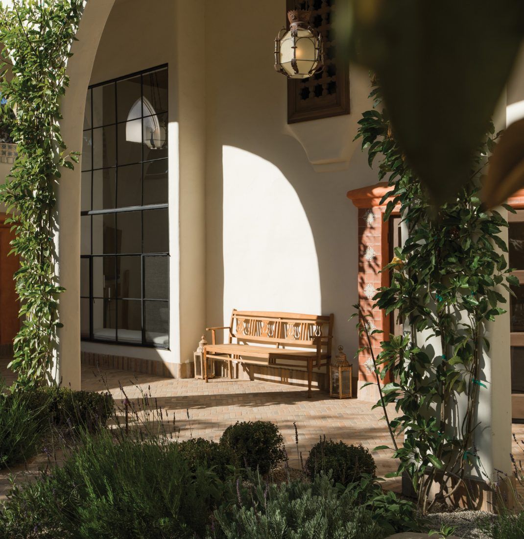 Arched stucco loggia with a hanging lantern, a wooden bench and clipped hedges in the courtyard beyond.