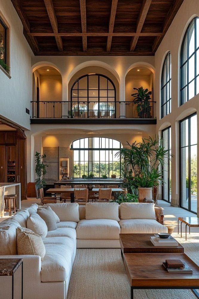 Double-height living room with an exposed wood-beam ceiling, tall arched windows, a white sectional sofa and large potted plants.